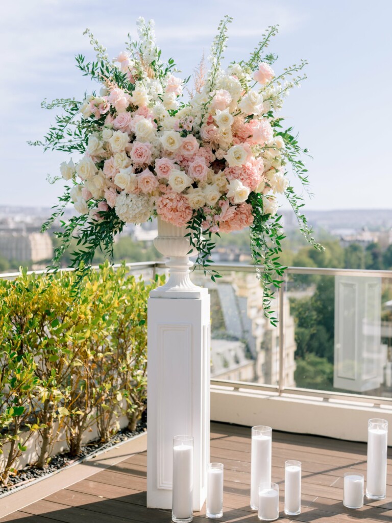 Grande composition florale sur colonne blanche, roses blanches et pêche, delphiniums et feuillage retombant, sur un rooftop parisien
